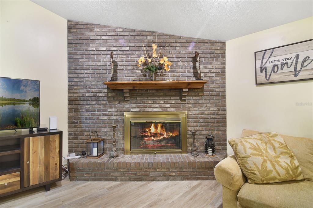 A living room features a brick fireplace with a wooden mantel and a television console — 1410 SE 44TH AVENUE, OCALA, FL
