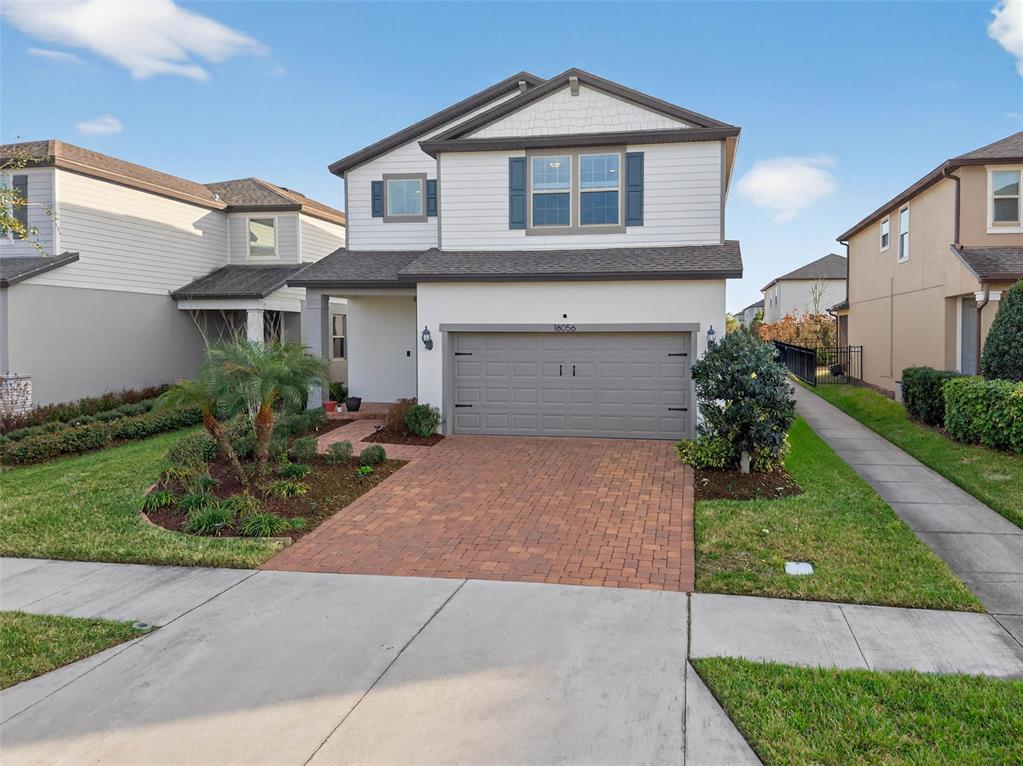 A two-story suburban house features a brick paver driveway, a garage, and white siding — 18056 AERO AVENUE, LAND O LAKES, FL