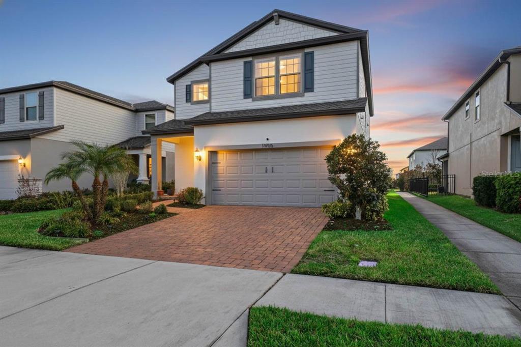 A two-story house with a brick paver driveway and a two-car garage at sunset — 18056 AERO AVENUE, LAND O LAKES, FL