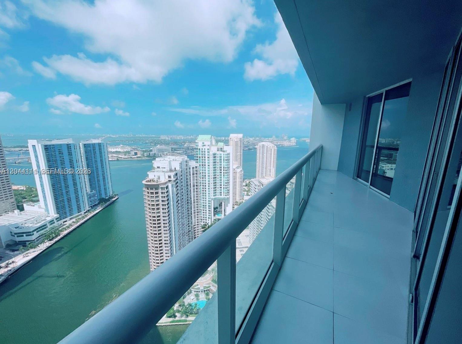 A high-rise balcony with glass railings overlooks a bay surrounded by modern city skyscrapers — 495 Brickell Ave # 4804, Miami FL 33131, MIAMI, FL