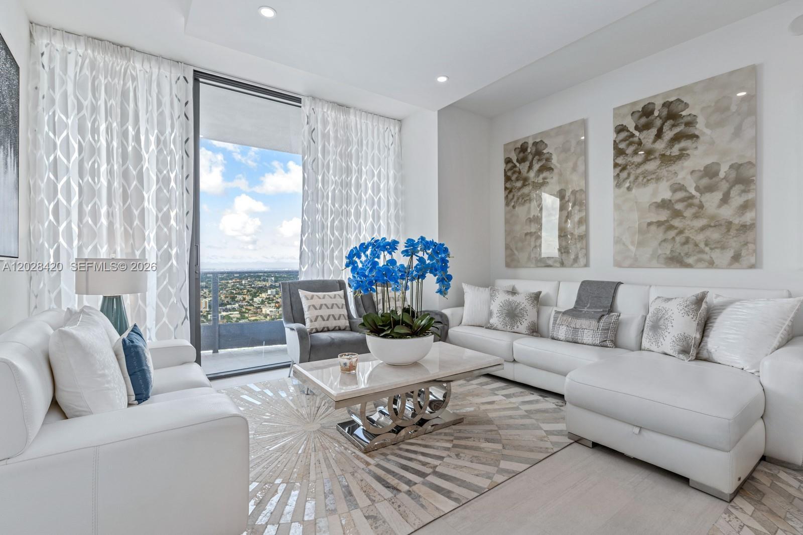 A modern living room features white leather sofas, a patterned rug, and floor-to-ceiling windows — 1000 Brickell Plz, Miami FL 33131, MIAMI, FL