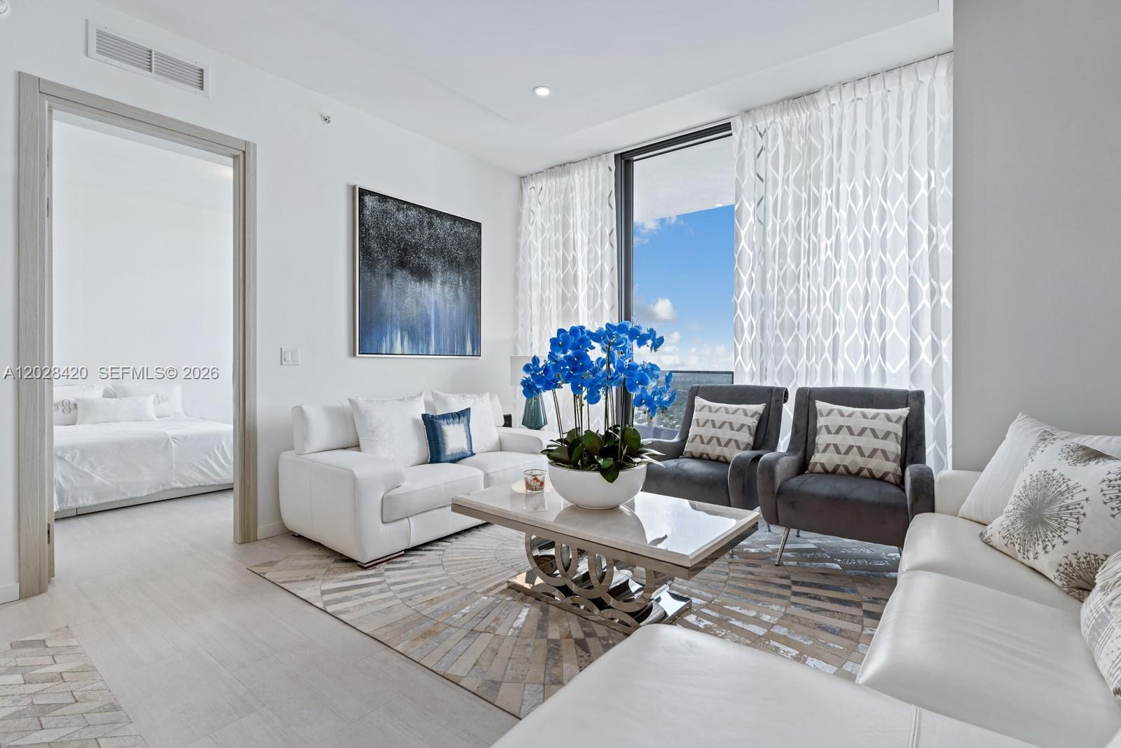 A modern living room features white sofas, gray armchairs, a patterned rug, and floor-to-ceiling windows — 1000 Brickell Plz, Miami FL 33131, MIAMI, FL