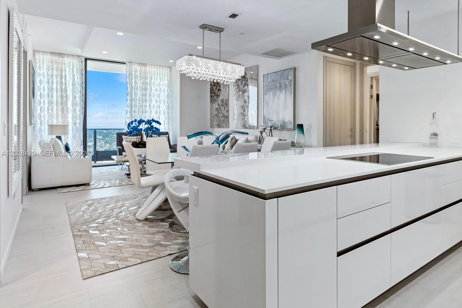 A modern white kitchen island overlooks a dining area and living room with floor-to-ceiling windows — 1000 Brickell Plz, Miami FL 33131, MIAMI, FL