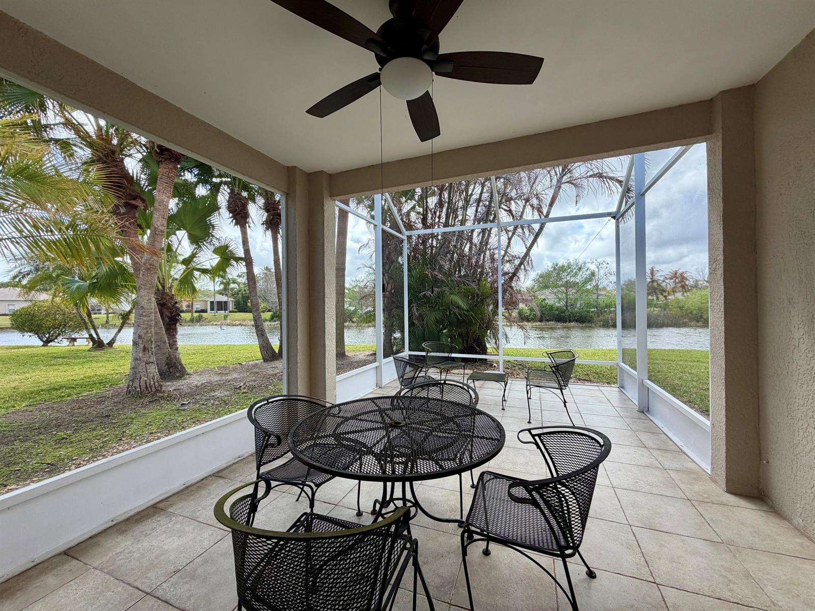 A screened-in patio features a metal dining set, ceiling fan, and views of a lake — 6295 33rd Manor, Vero Beach FL 32966, VERO BEACH, FL
