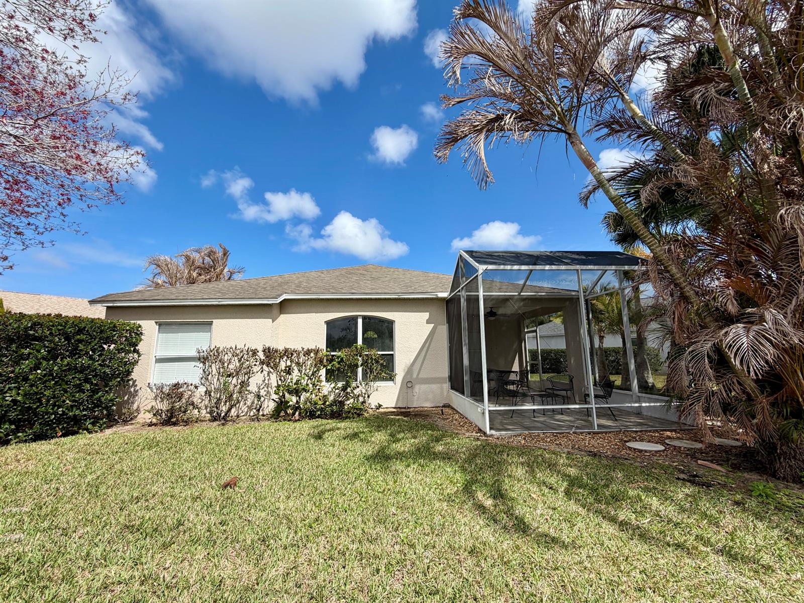 The exterior of a beige house features a screened-in patio and a grassy backyard — 6295 33rd Manor, Vero Beach FL 32966, VERO BEACH, FL