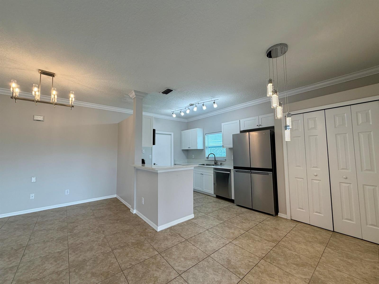 A kitchen with white cabinets, stainless steel appliances, and tile flooring opens to a dining area — 6295 33rd Manor, Vero Beach FL 32966, VERO BEACH, FL