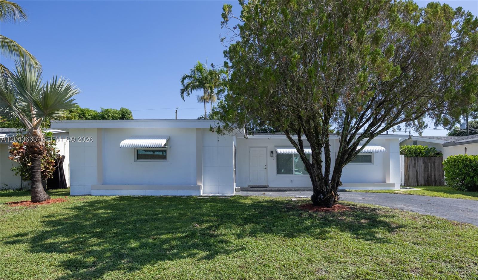 A single-story white house features a front lawn, a large tree, and metal awnings — 8571 NW 27th Pl, Sunrise FL 33322, SUNRISE, FL
