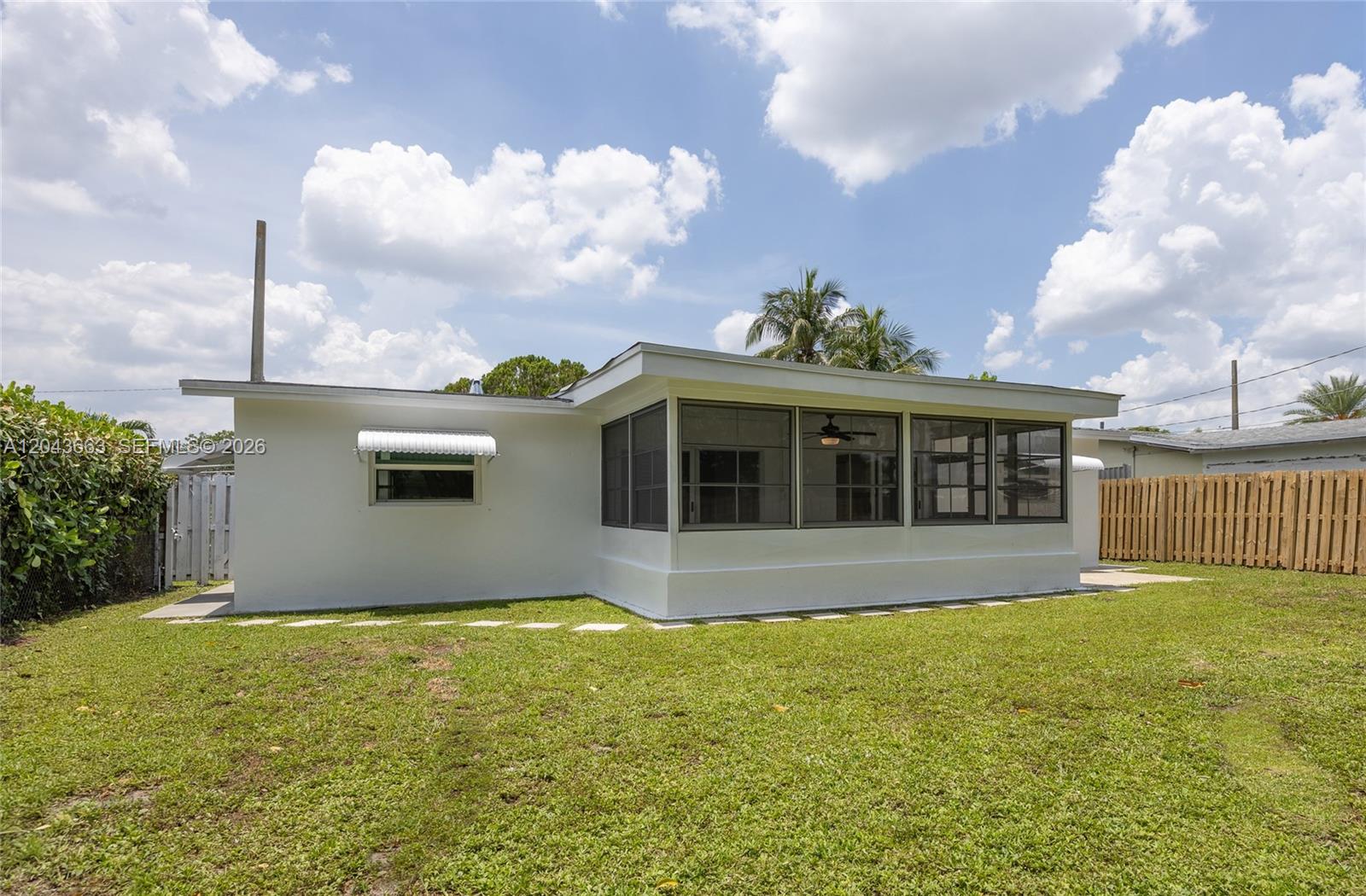 The exterior of a white house features a screened-in porch and a grassy backyard — 8571 NW 27th Pl, Sunrise FL 33322, SUNRISE, FL