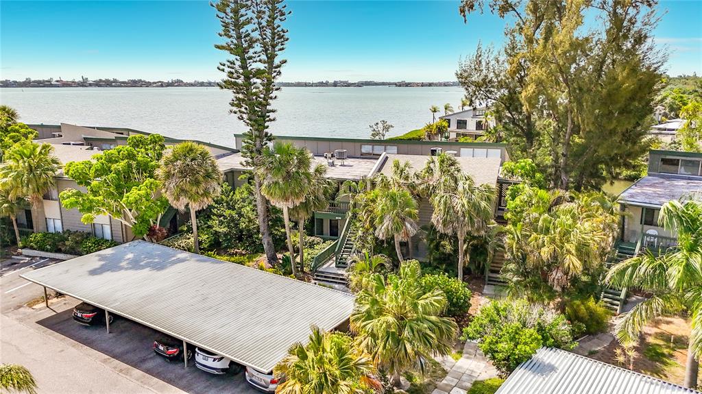An elevated view of a multi-story apartment complex with palm trees and a covered parking area — 1515 PELICAN POINT DRIVE UNIT BA185, SARASOTA, FL