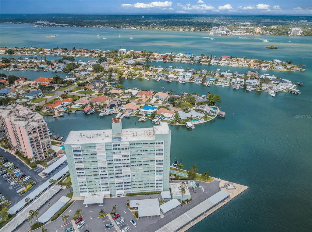 An aerial view shows a tall apartment building situated on a waterfront peninsula — 31 ISLAND WAY UNIT 605, CLEARWATER BEACH, FL