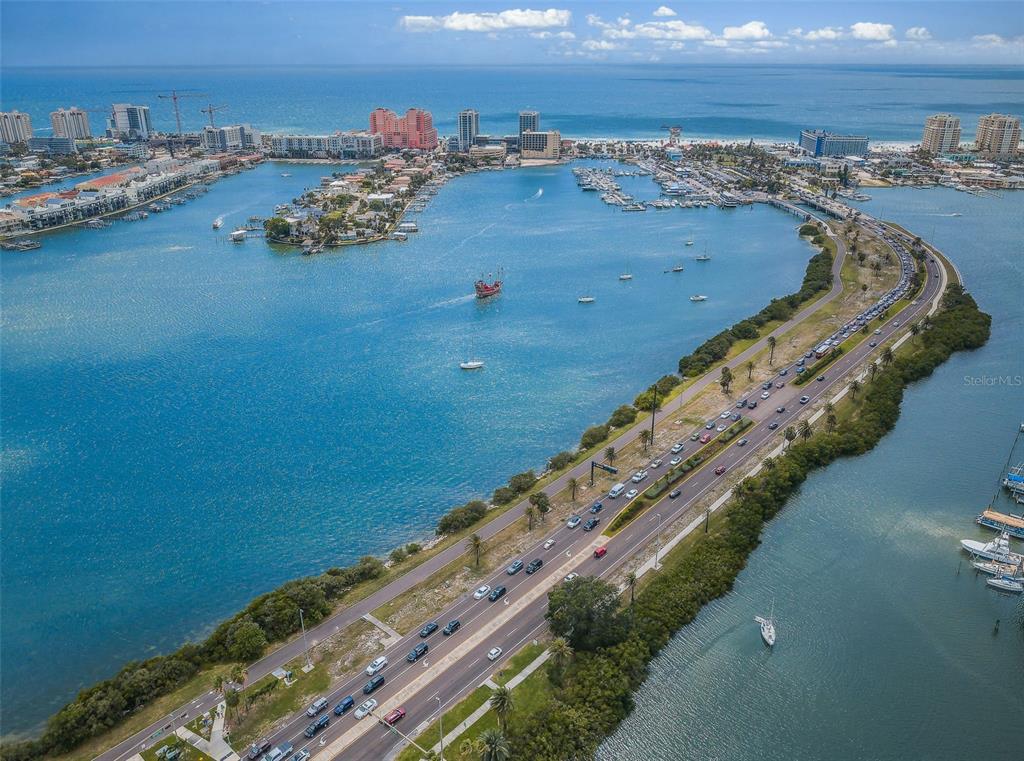 An aerial view shows a coastal road curving along a bay with boats and buildings — 31 ISLAND WAY UNIT 605, CLEARWATER BEACH, FL