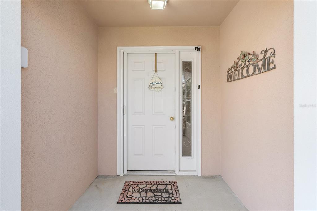 A white front door with a side light and welcome signs sits in a covered entryway — 14160 SE 85TH AVENUE, SUMMERFIELD, FL