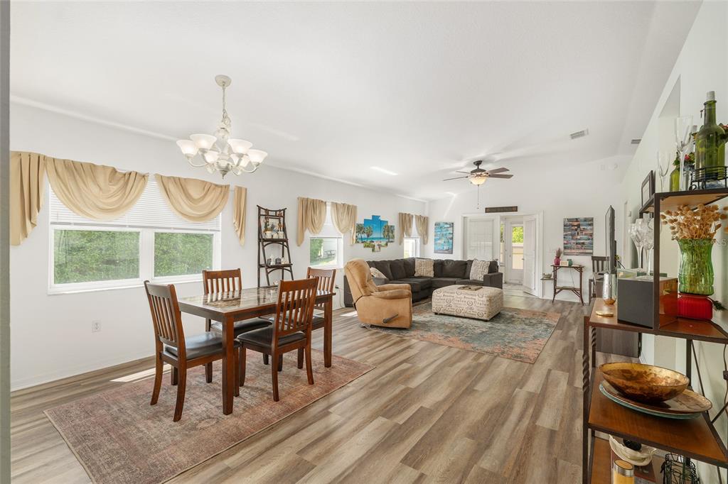 An open-concept living and dining room with wood-look flooring, a chandelier, and neutral walls — 14160 SE 85TH AVENUE, SUMMERFIELD, FL