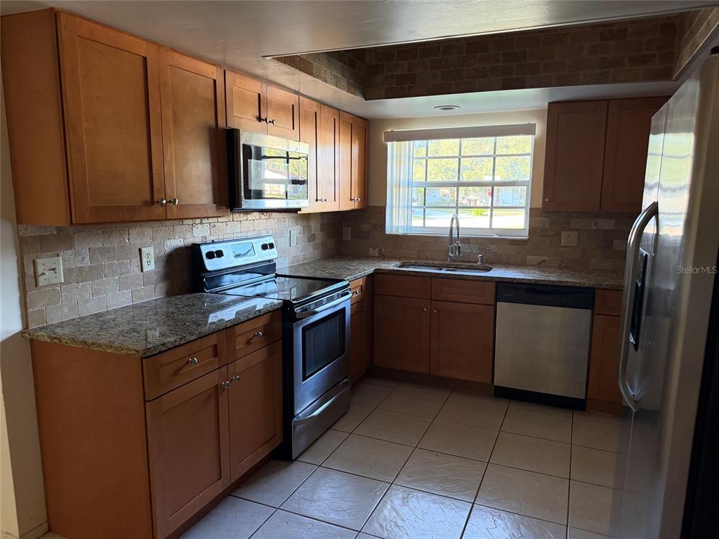 A kitchen features wood cabinets, granite countertops, stainless steel appliances, and a tiled floor — 4805 LANDOVER CIRCLE, ORLANDO, FL