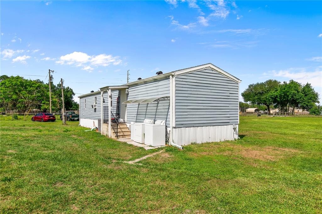 A light blue mobile home sits in a grassy field with outdoor laundry appliances — 3834 HIXON AVENUE, ST CLOUD, FL