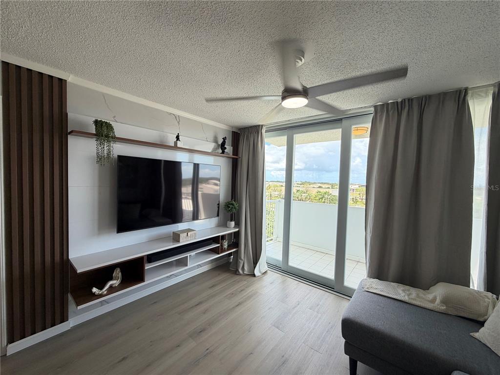 A living room features a wall-mounted television, custom shelving, wood-look flooring, and a balcony view — 190 MARGINAL LOS ANGELES UNIT 8, CAROLINA, PR
