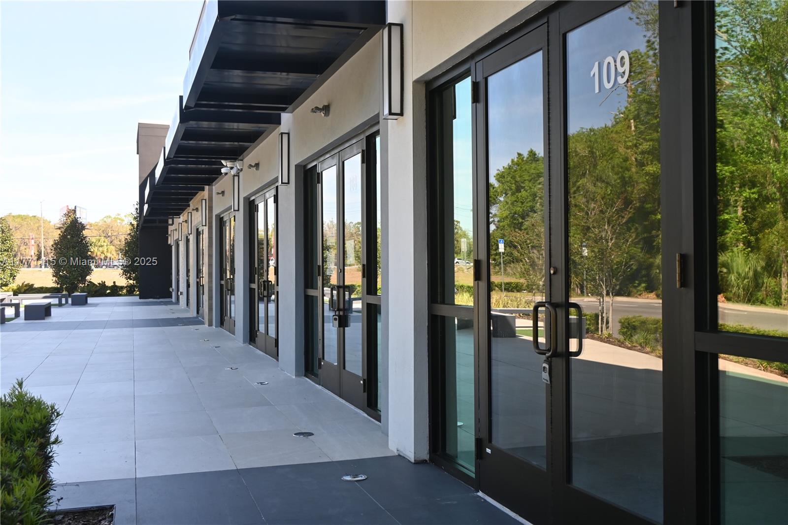 A row of glass storefront doors with black frames lines a paved outdoor walkway — 3370 ROUSE RD # 109, Orlando FL 32817, ORLANDO, FL