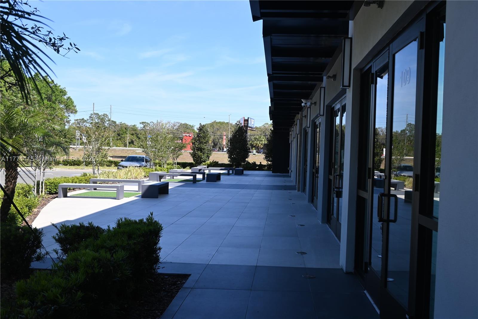 A paved outdoor walkway features modern benches and glass storefronts under a covered overhang — 3370 ROUSE RD # 109, Orlando FL 32817, ORLANDO, FL