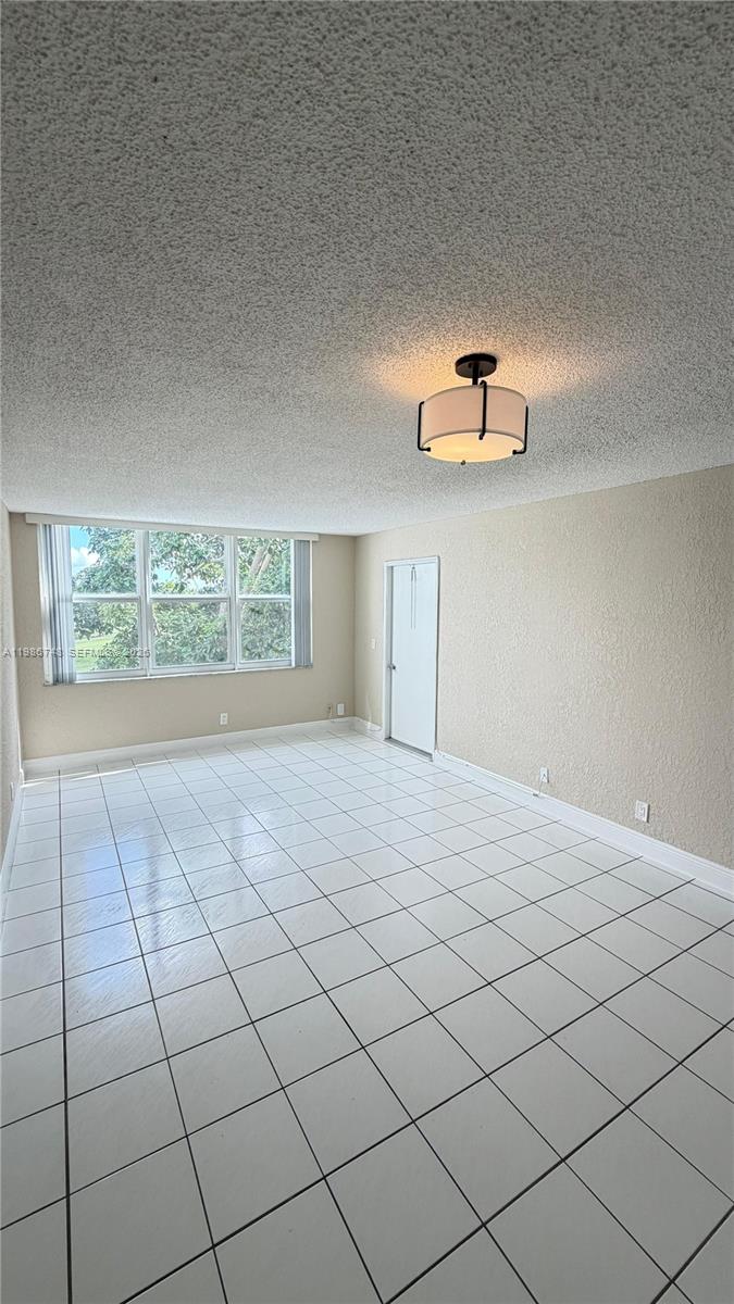 An empty room features white tile flooring, a textured ceiling, and a modern drum light — 9461 Evergreen Pl # 305, Davie FL 33324, DAVIE, FL