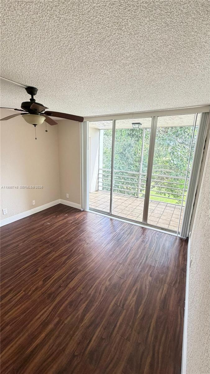 An empty room with dark wood-look flooring, a ceiling fan, and sliding glass balcony doors — 9461 Evergreen Pl # 305, Davie FL 33324, DAVIE, FL