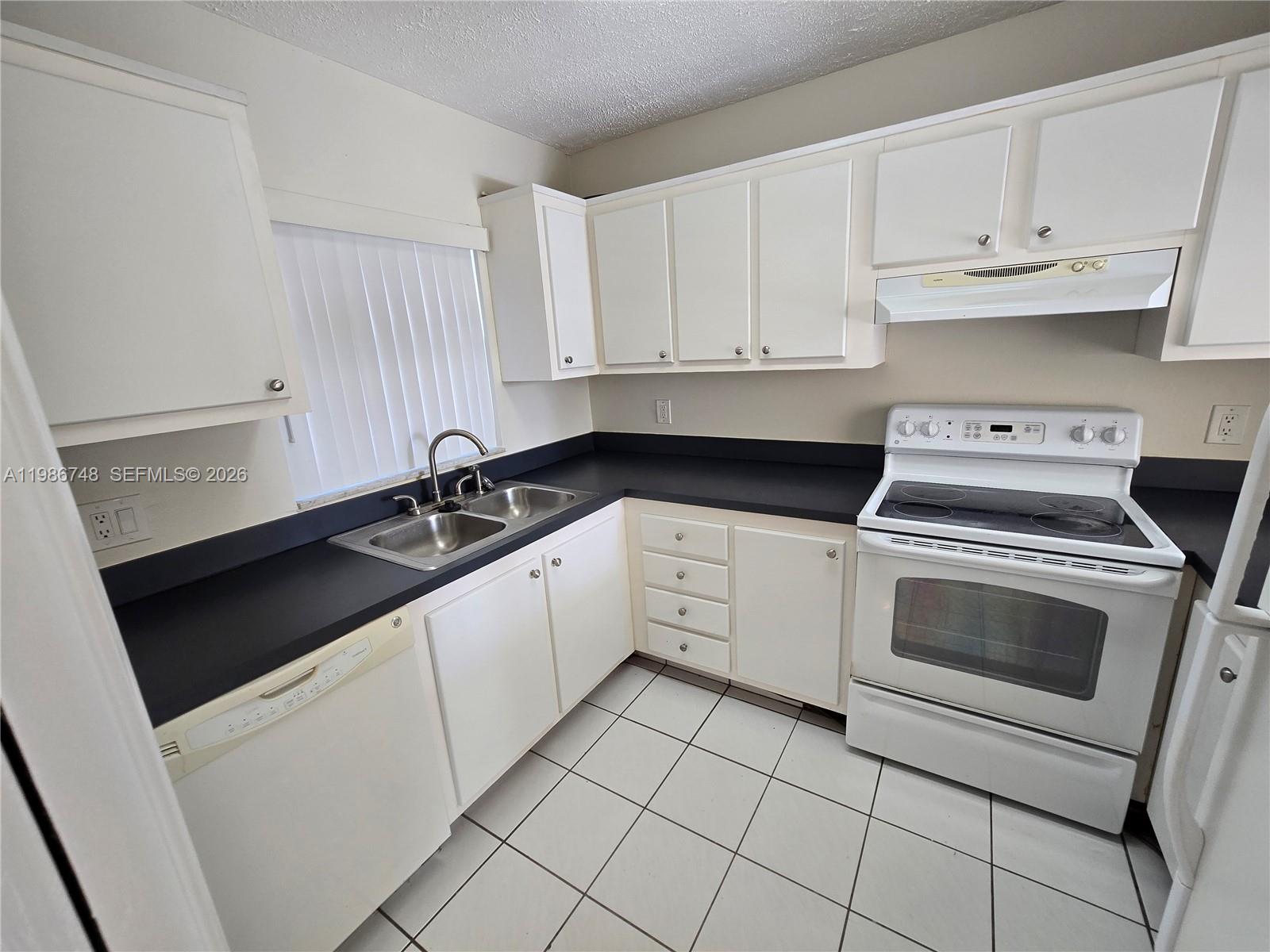 A kitchen features white cabinets, black countertops, white appliances, and white floor tiles — 9461 Evergreen Pl # 305, Davie FL 33324, DAVIE, FL