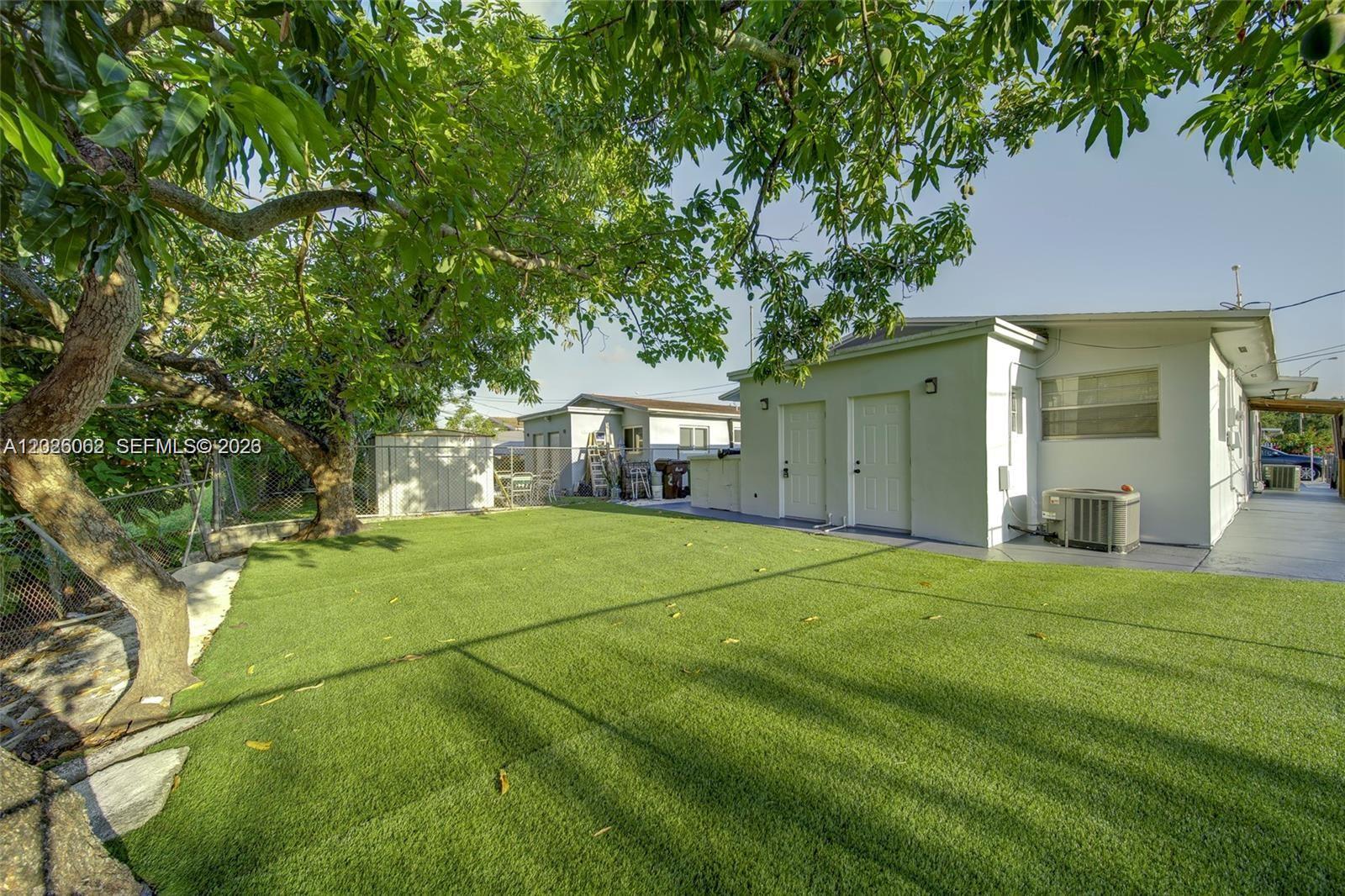 A backyard features artificial turf, a large tree, and the exterior of a white house — 896 E 22nd St # 898, Hialeah FL 33013, HIALEAH, FL