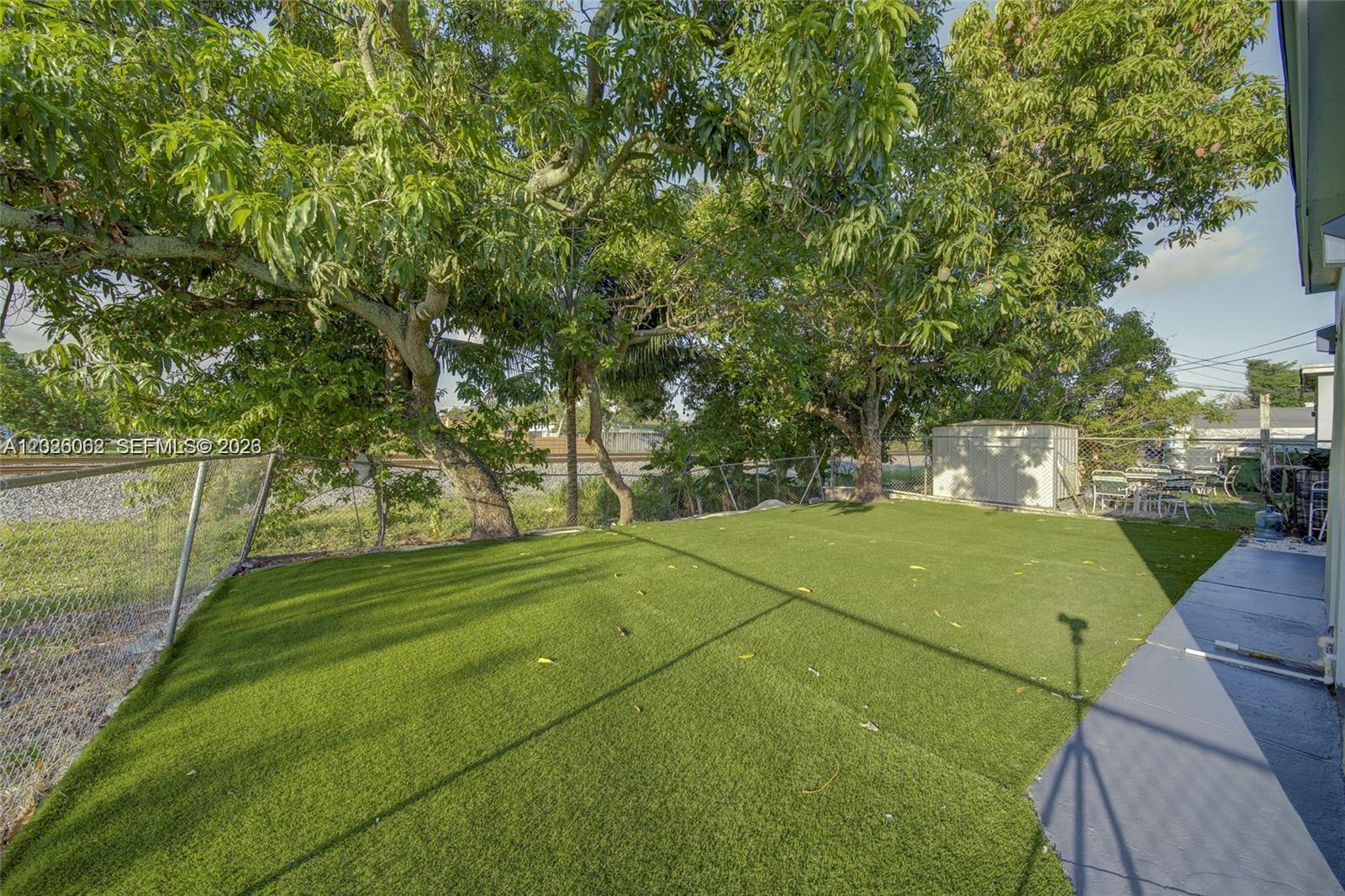 A backyard features artificial turf, mature trees, a chain-link fence, and a storage shed — 896 E 22nd St # 898, Hialeah FL 33013, HIALEAH, FL