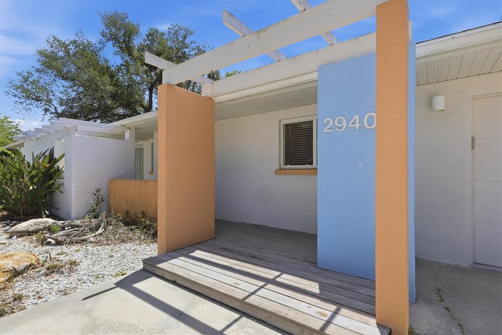 A wooden deck leads to an entrance framed by blue and peach-colored stucco walls — 2940 BOUGAINVILLEA STREET, SARASOTA, FL