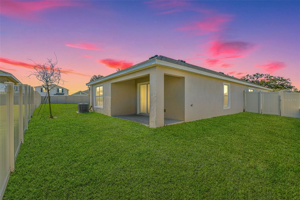 A view of a house exterior with a covered patio, lawn, and vinyl fencing — 13581 MOUNT IVY COURT, DADE CITY, FL
