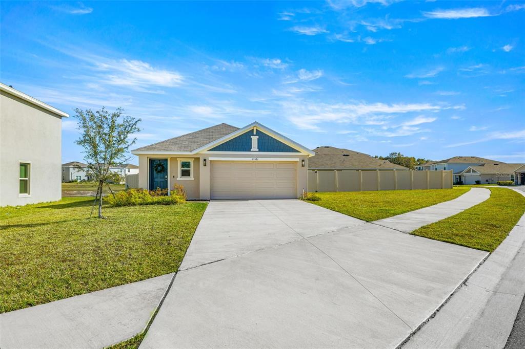 A single-story house with a beige exterior, blue front door, and a two-car garage — 13581 MOUNT IVY COURT, DADE CITY, FL