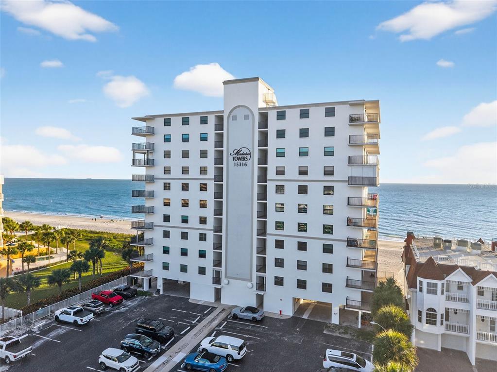 An aerial view of a multi-story beachfront condominium building with an adjacent parking lot — 15316 GULF BOULEVARD UNIT 903, MADEIRA BEACH, FL