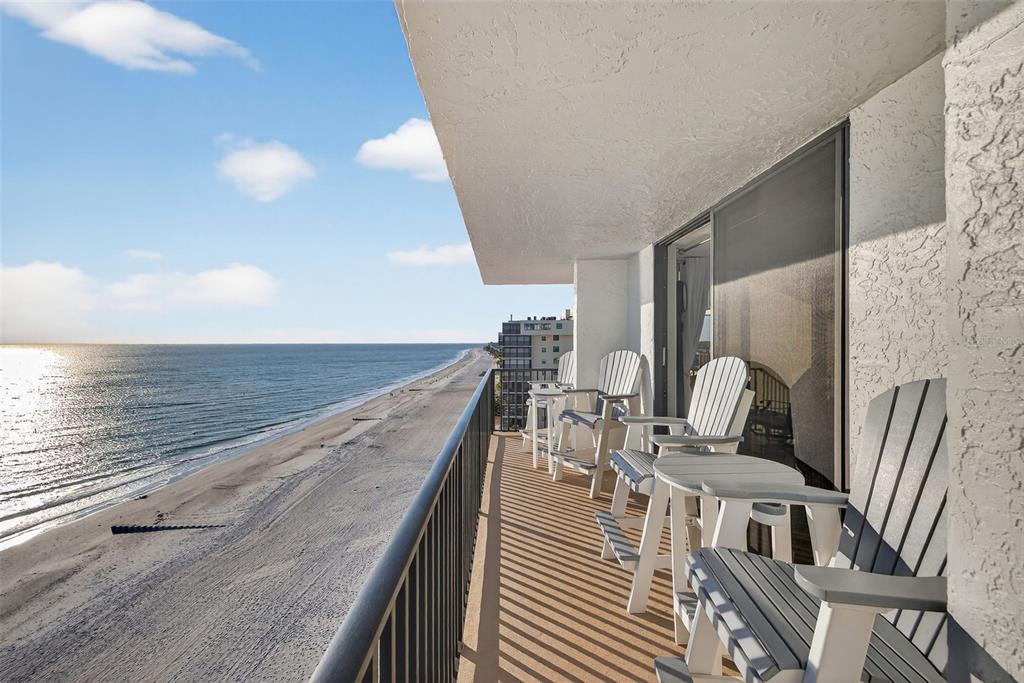 A balcony with patio chairs overlooks a sandy beach and the ocean under a blue sky — 15316 GULF BOULEVARD UNIT 903, MADEIRA BEACH, FL
