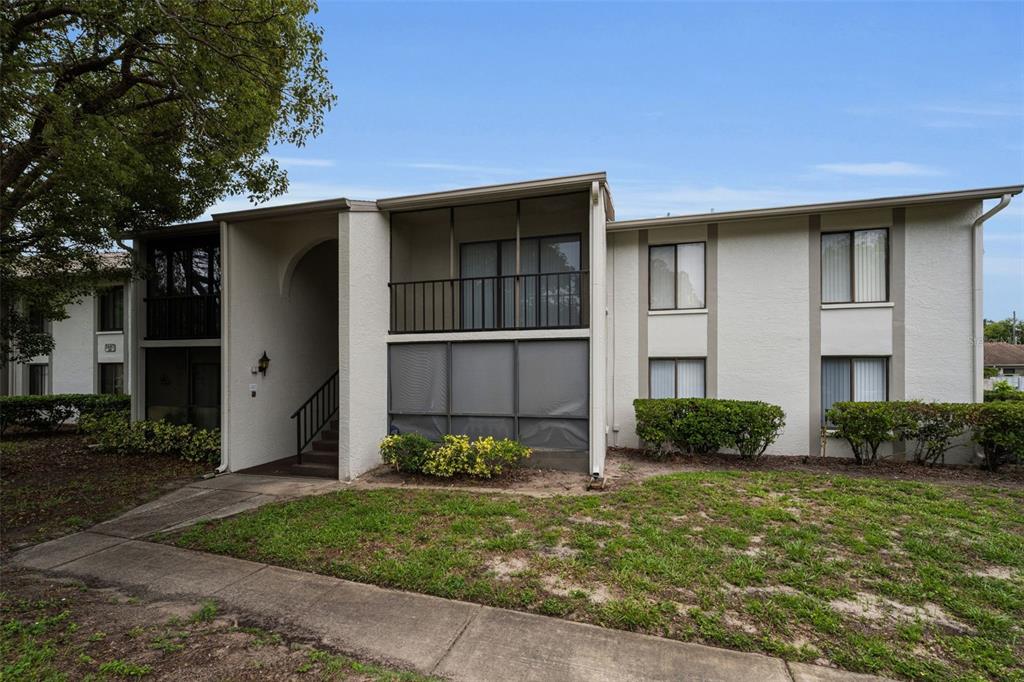 A two-story apartment building features a screened balcony, ground-floor patio, and a shared entryway — 2687 PINE RIDGE WAY S UNIT B2, PALM HARBOR, FL