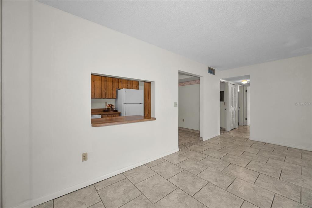 A room with light-colored tile flooring features a kitchen pass-through window with a wooden counter — 2687 PINE RIDGE WAY S UNIT B2, PALM HARBOR, FL