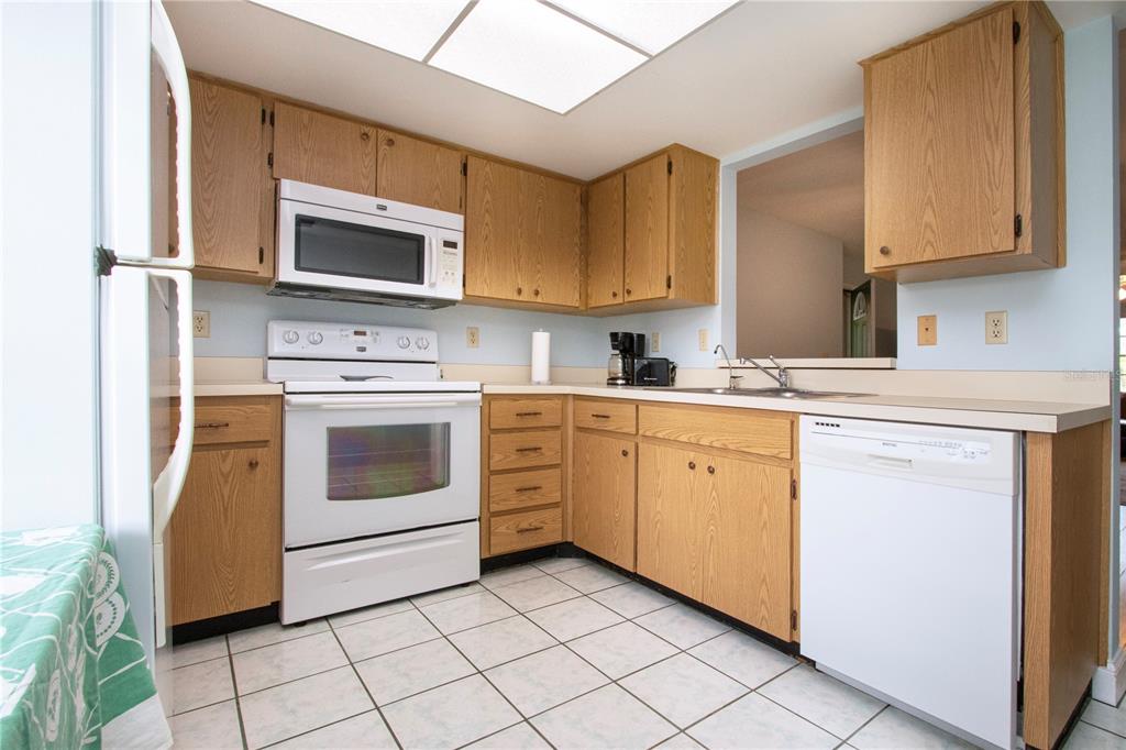 A kitchen features oak cabinets, white appliances, a tiled floor, and a pass-through window — 2017 HULLHOUSE DRIVE UNIT 351, SUN CITY CENTER, FL