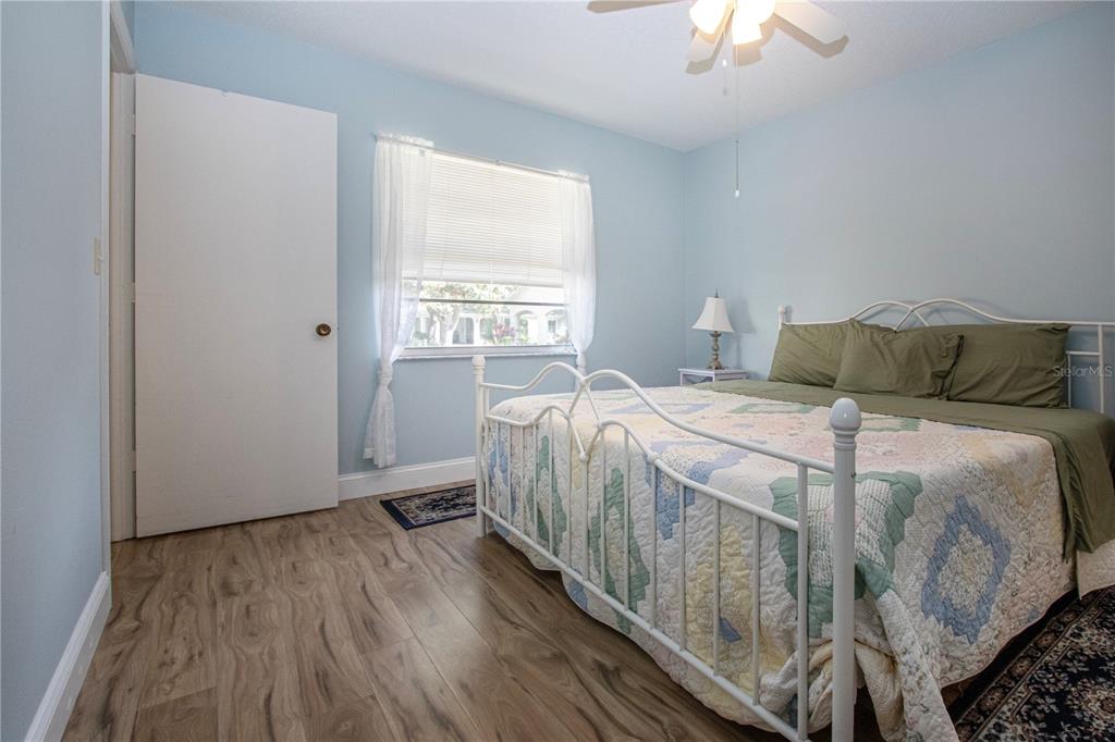 A bedroom features light blue walls, wood-look flooring, a white metal bed frame, and a window — 2017 HULLHOUSE DRIVE UNIT 351, SUN CITY CENTER, FL