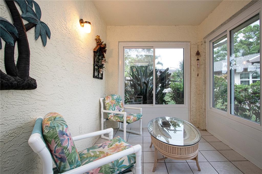 A sunroom features tile floors, two floral-patterned chairs, a glass-top coffee table, and large windows — 2017 HULLHOUSE DRIVE UNIT 351, SUN CITY CENTER, FL