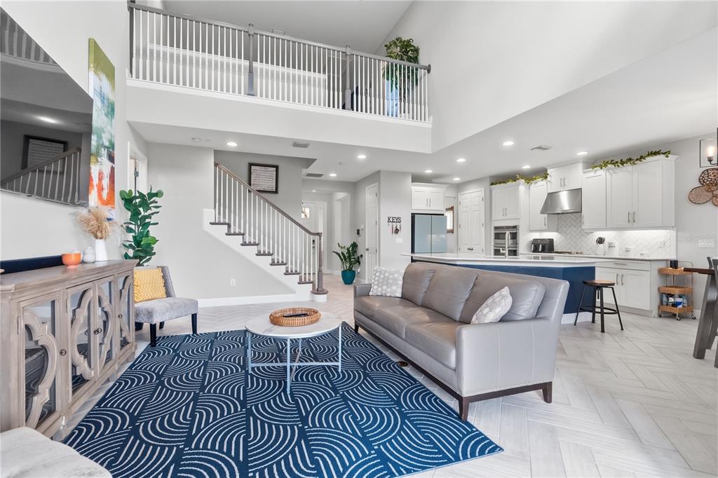A living room with a grey sofa, blue patterned rug, and stairs leading to a loft — 4939 LOS ROBLES COURT, PALMETTO, FL