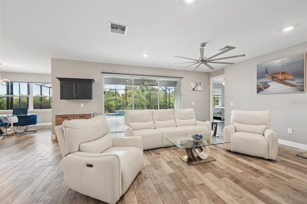 A living room with white leather furniture, wood-look tile flooring, and a sliding glass door — 15301 CHINOOK WAY, PORT CHARLOTTE, FL