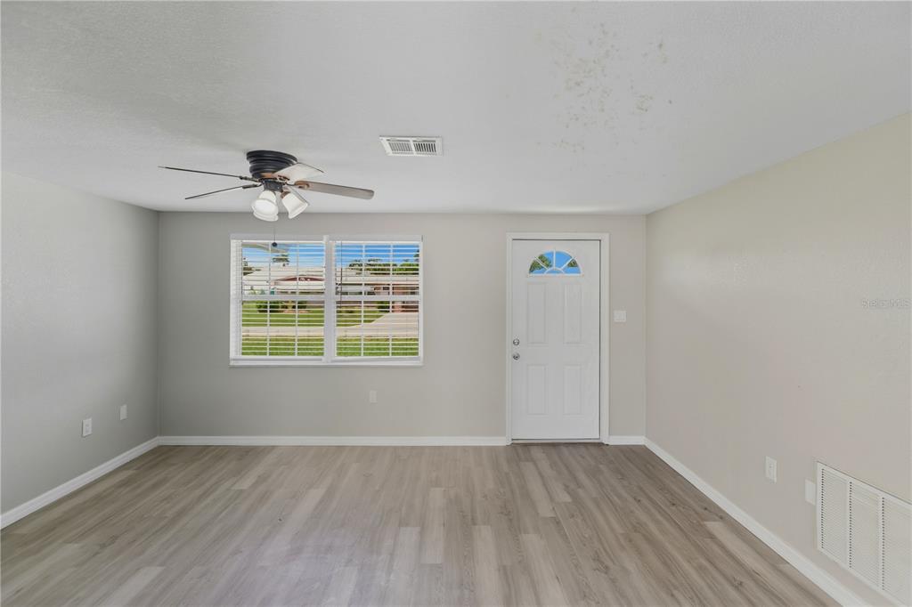 An empty room features light gray walls, wood-look flooring, a ceiling fan, and a front door — 185 SALEM AVENUE NW, PORT CHARLOTTE, FL