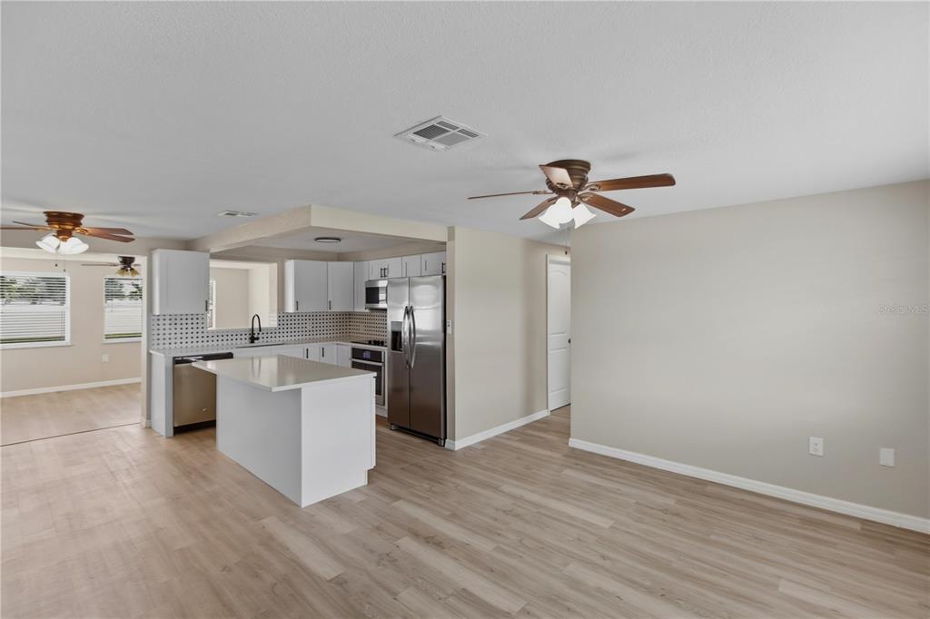 A kitchen with white cabinets, stainless steel appliances, and an island opens to a living area — 185 SALEM AVENUE NW, PORT CHARLOTTE, FL