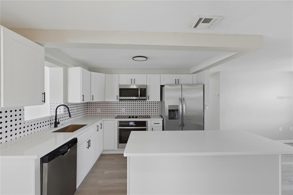 A modern kitchen features white cabinets, stainless steel appliances, and a patterned backsplash — 185 SALEM AVENUE NW, PORT CHARLOTTE, FL