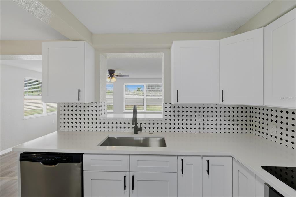 A kitchen features white cabinets, a stainless steel sink, and a black-and-white patterned backsplash — 185 SALEM AVENUE NW, PORT CHARLOTTE, FL