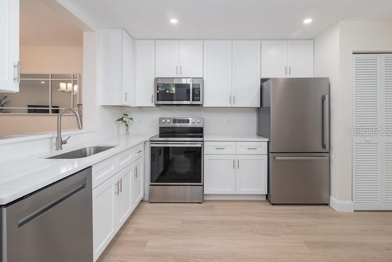 A kitchen features white cabinets, stainless steel appliances, and light wood flooring — 223 LAKEWOOD DRIVE UNIT 223, BRADENTON, FL