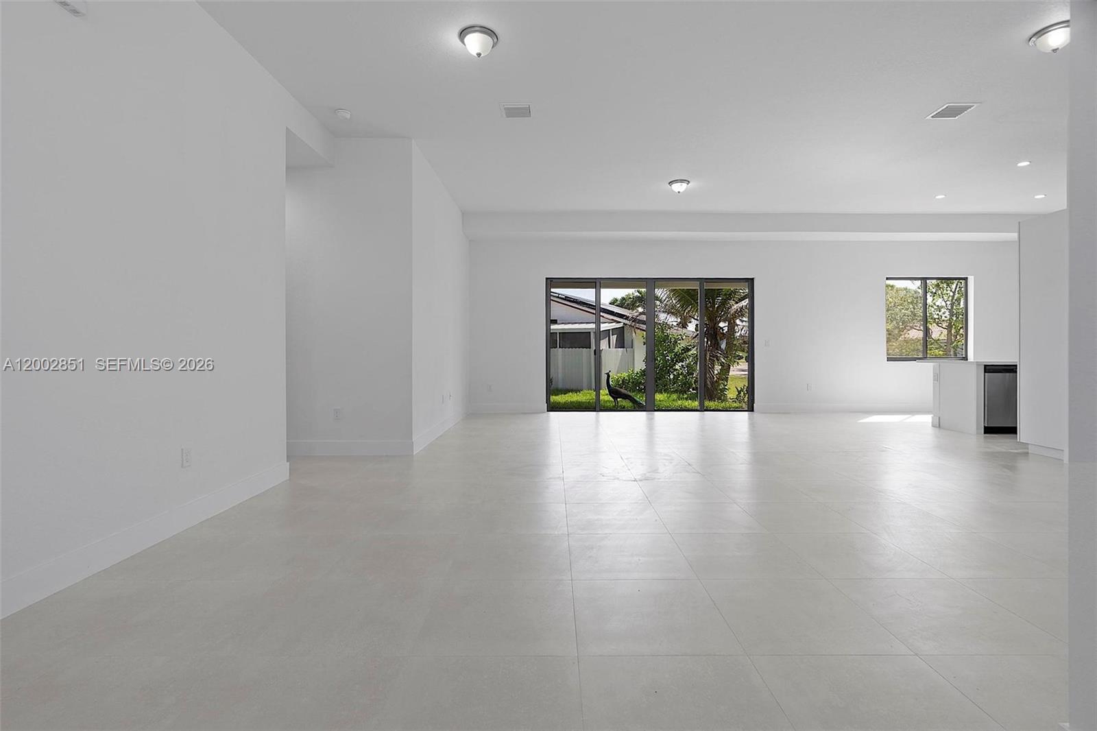A spacious, white-tiled living area features large glass sliding doors and a view of a peacock — 20943 SW 96th Ct, Cutler Bay FL 33189, CUTLER BAY, FL