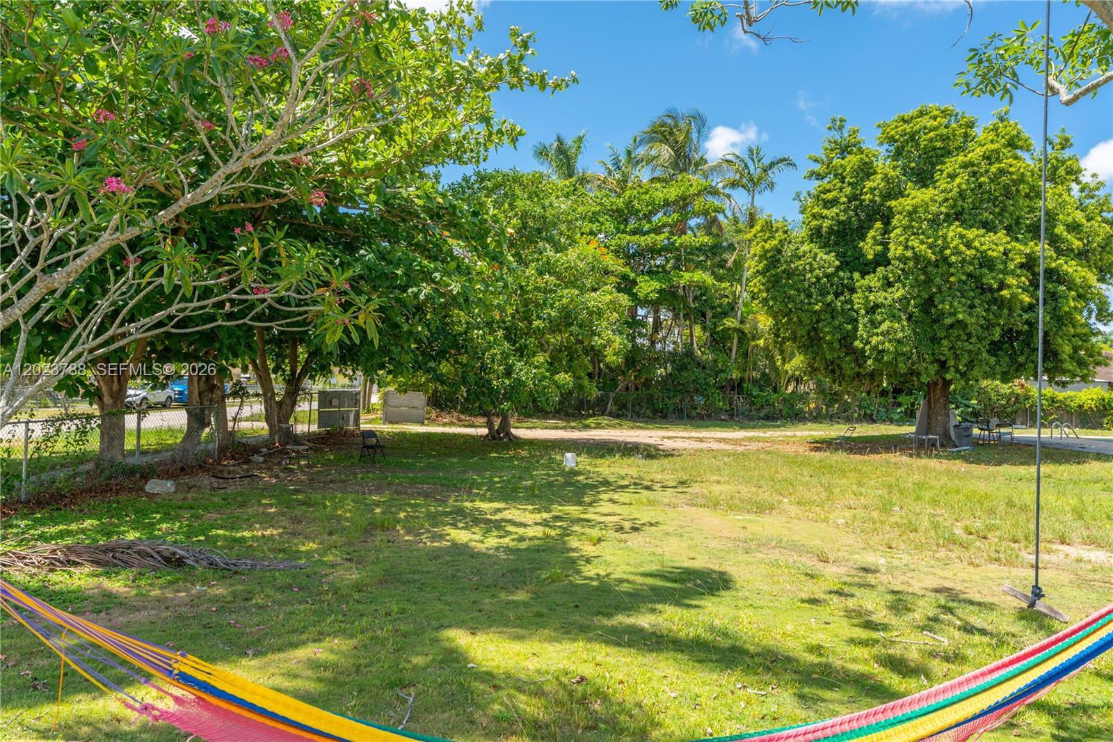 A grassy backyard features a colorful hammock in the foreground and mature trees — 329 NW 13th St, Homestead FL 33030, HOMESTEAD, FL