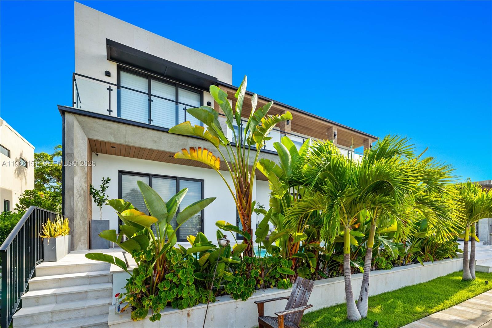 A modern two-story house features a balcony, large windows, and lush tropical landscaping — 2050 S Hibiscus Dr, North Miami FL 33181, NORTH MIAMI, FL