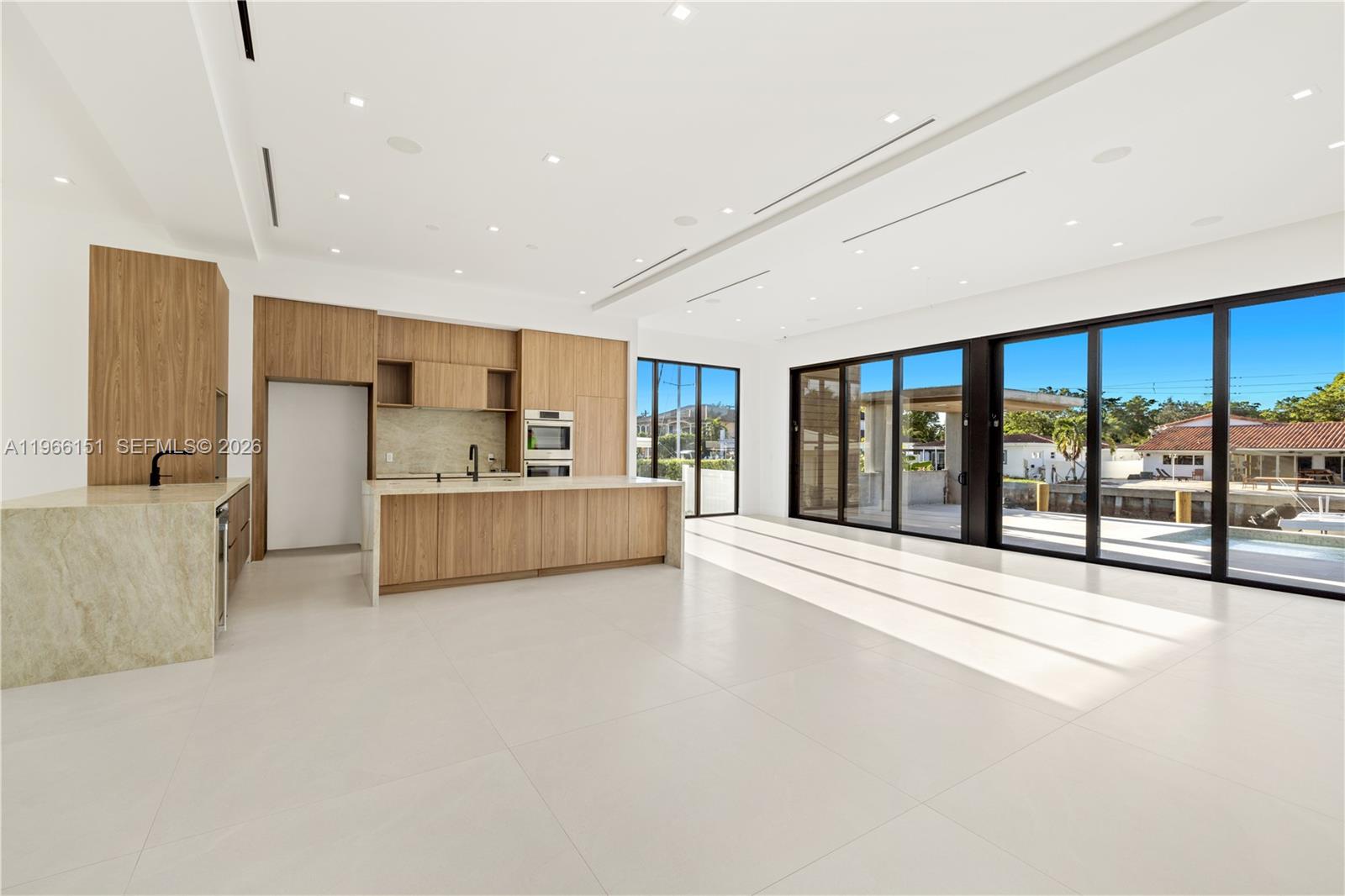 A modern kitchen features light wood cabinetry, a stone island, and large floor-to-ceiling windows — 2050 S Hibiscus Dr, North Miami FL 33181, NORTH MIAMI, FL