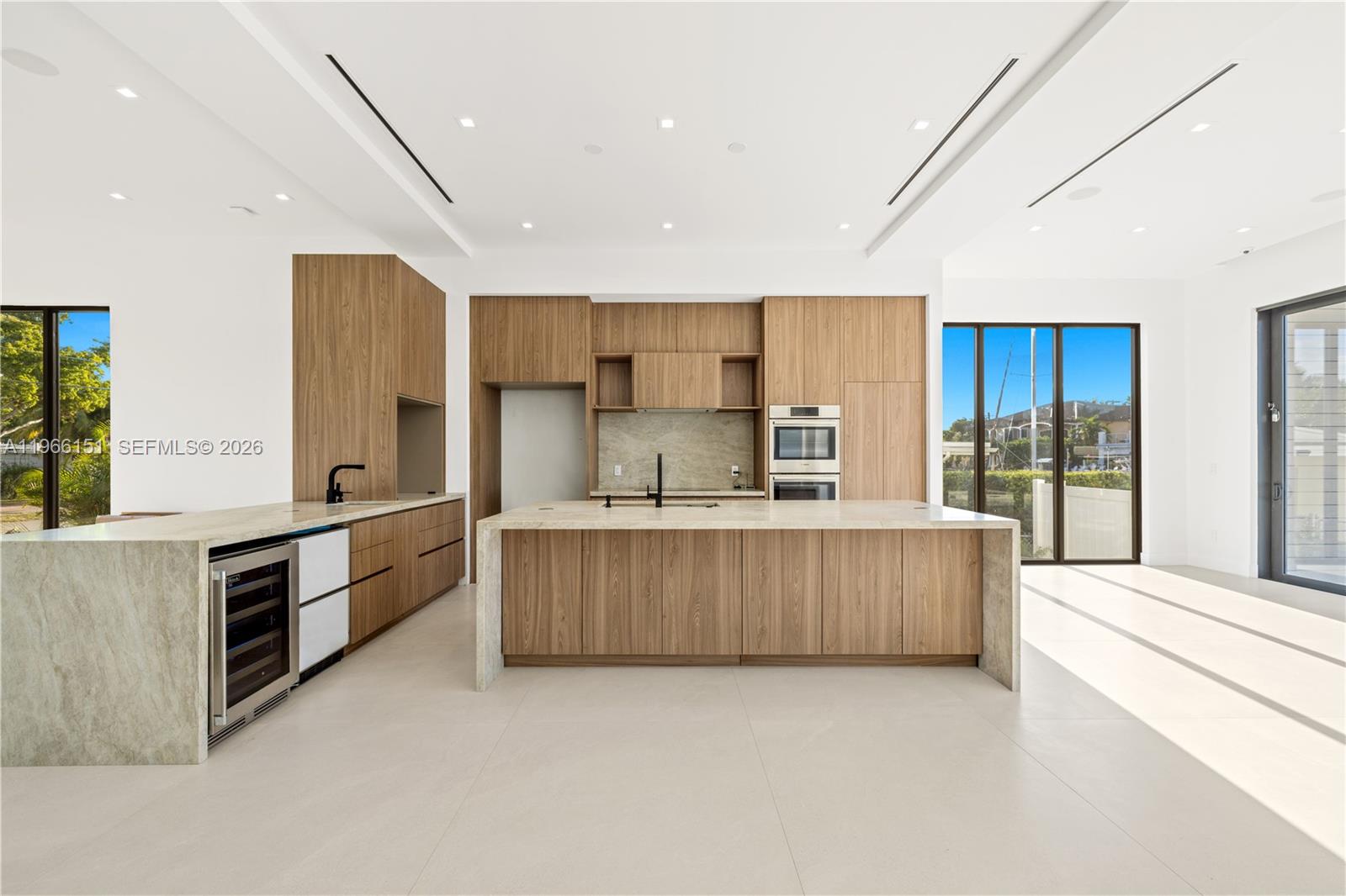 A modern kitchen features wood cabinetry, a large stone island, and floor-to-ceiling windows — 2050 S Hibiscus Dr, North Miami FL 33181, NORTH MIAMI, FL
