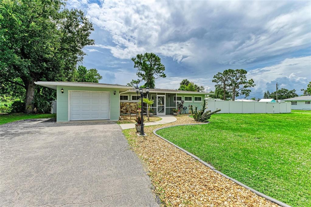 A single-story house with a light green exterior, a white garage door, and a gravel yard — 557 READING STREET NW, PORT CHARLOTTE, FL